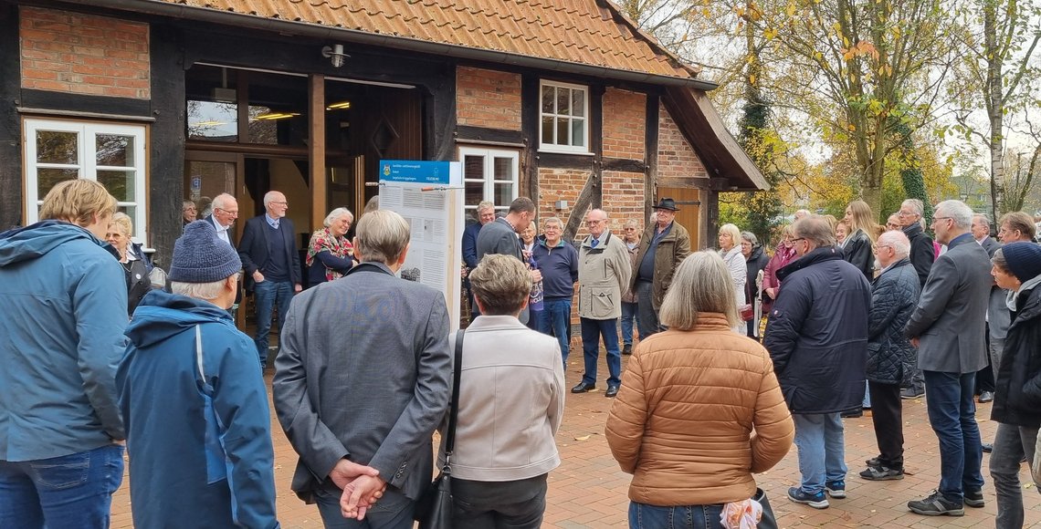 Zahlreiche Menschen stehen im Kreis um die Geschichts- und Erinnerungstafeln. Im Hintergrund ein Fachwerkhaus.