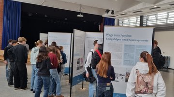 Schülerinnen und Schüler stehen in einem großen Raum vor Ausstellungswänden und betrachten diese.